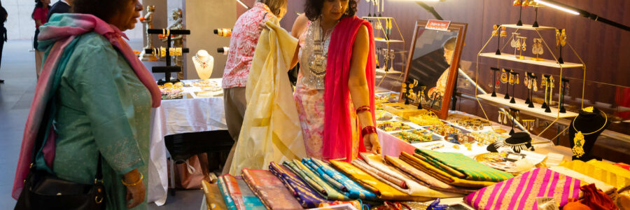 Individuals shopping at a vendor booth with jewelry and colorful clothing laid out.